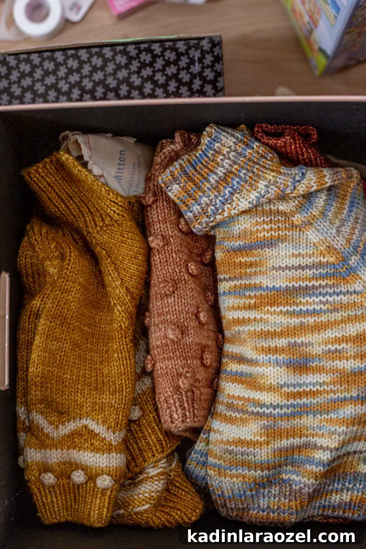 hand knit sweaters for babies, folded up in a box, ready to be organized