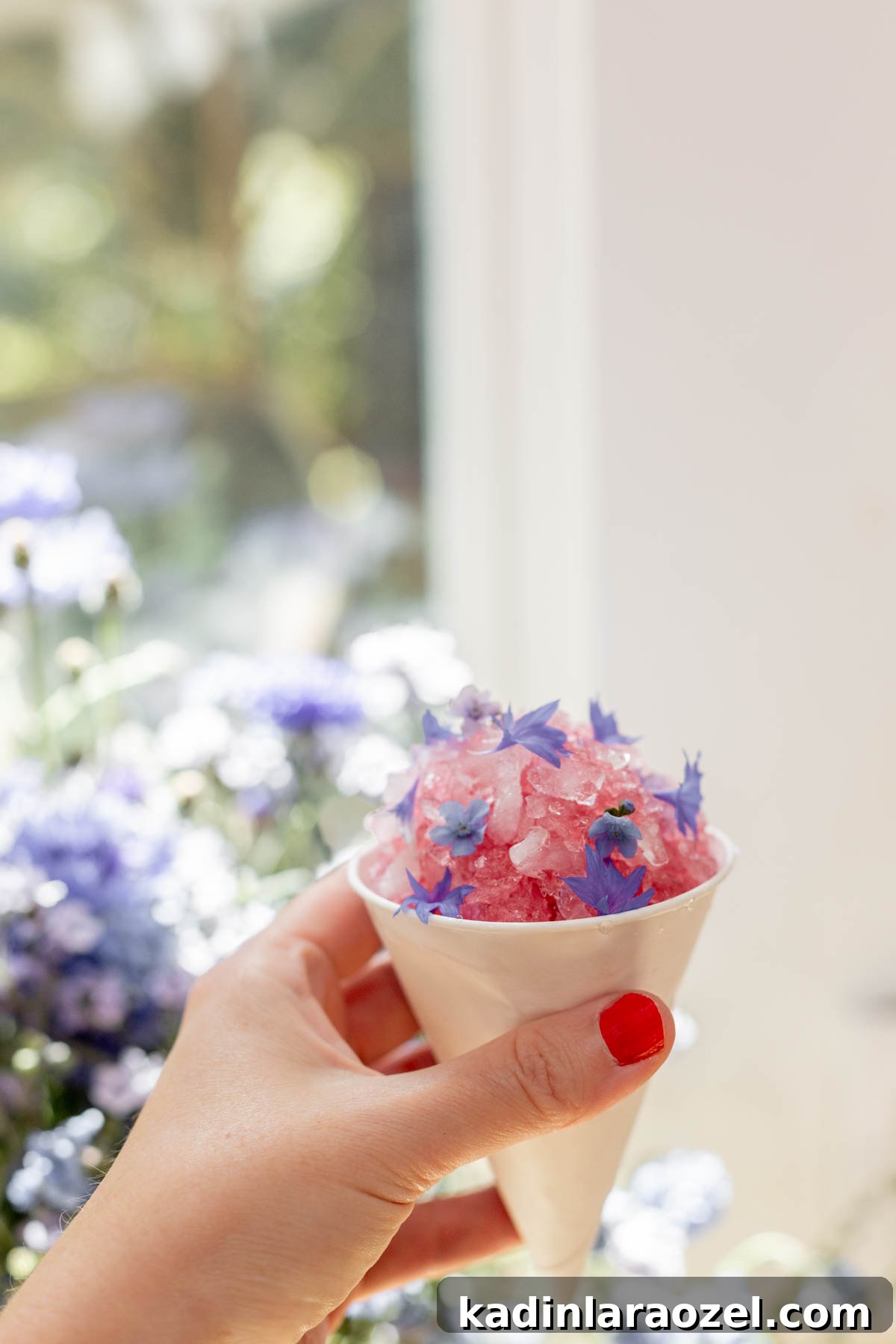 Three-Ingredient Blackberry Syrup Recipe for Pancakes and Desserts 9 woman holding pink snow cone near a sunny window, with purple edible flowers on top