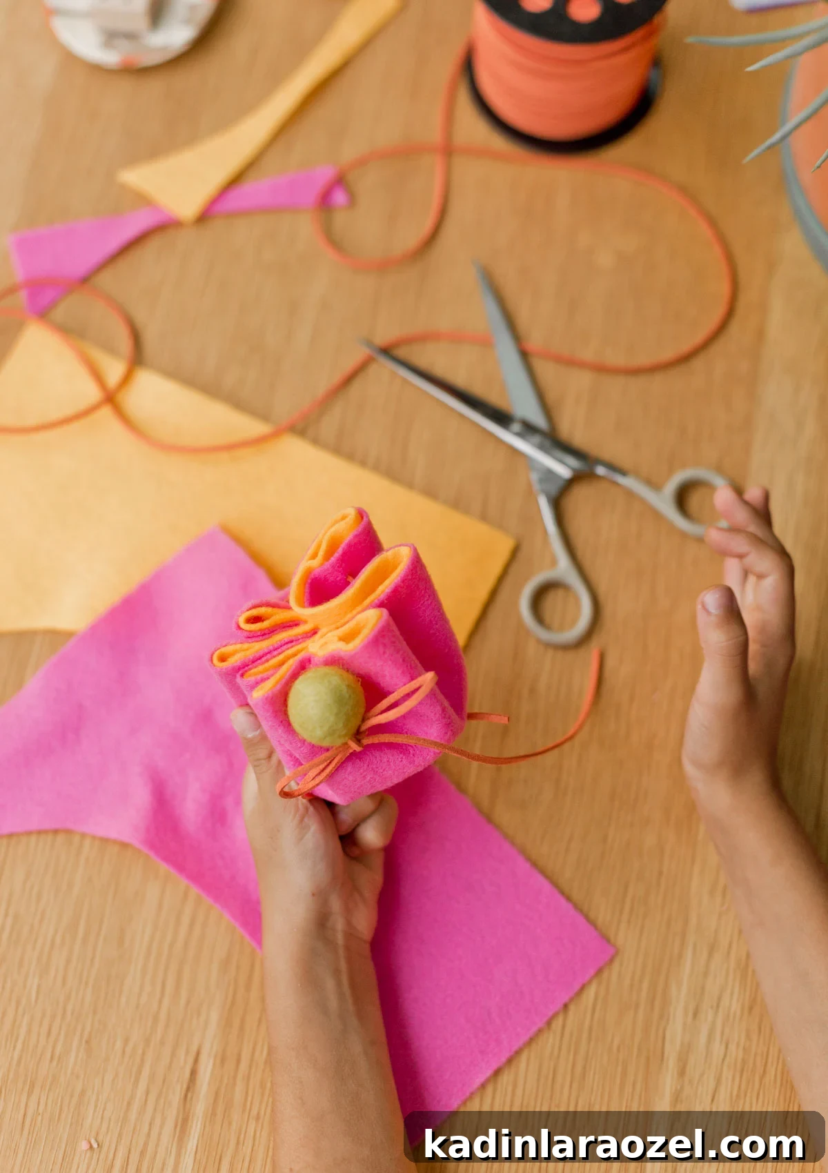 DIY Drawstring Pouch: Step-by-Step Sewing Tutorial 11 child's hand holding colorful pink and orange felt pouch, with craft supplies all around on the table