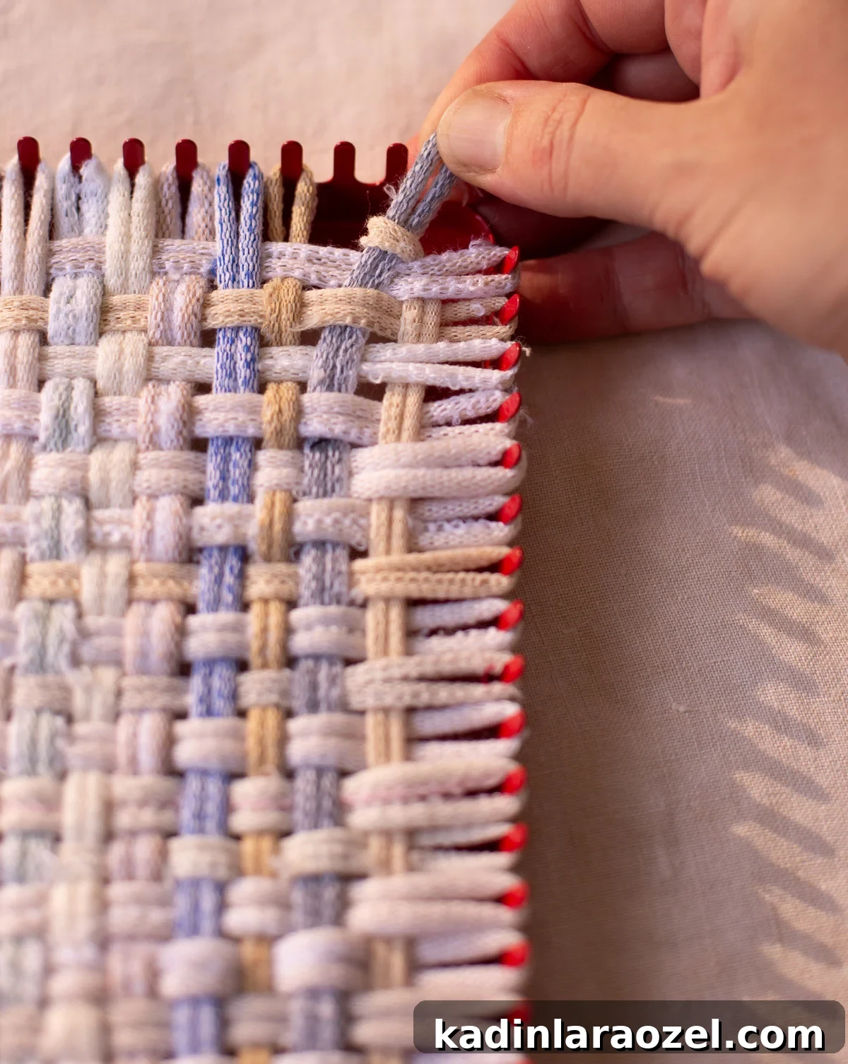 woman finishing a weaving with her hands on small square loom