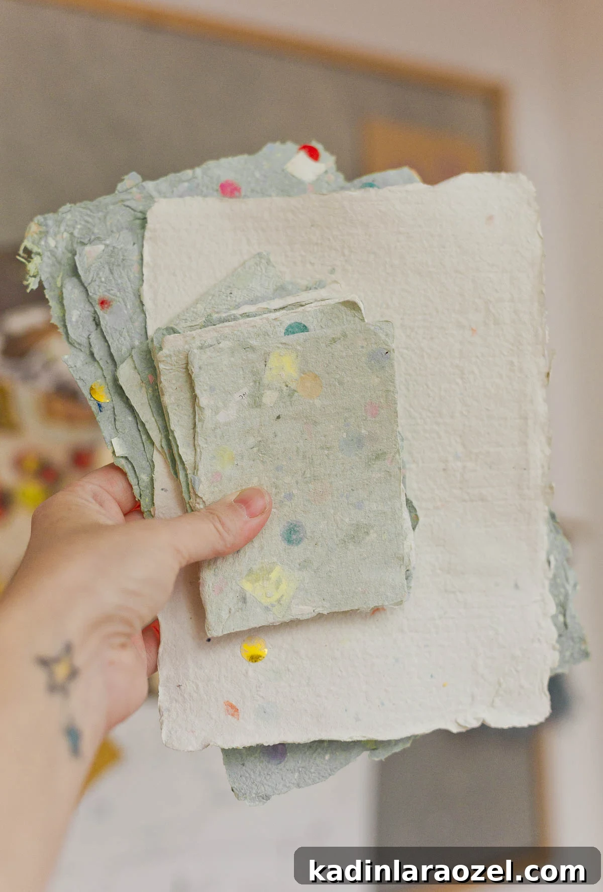 holding up homemade paper in different colors, in a stack