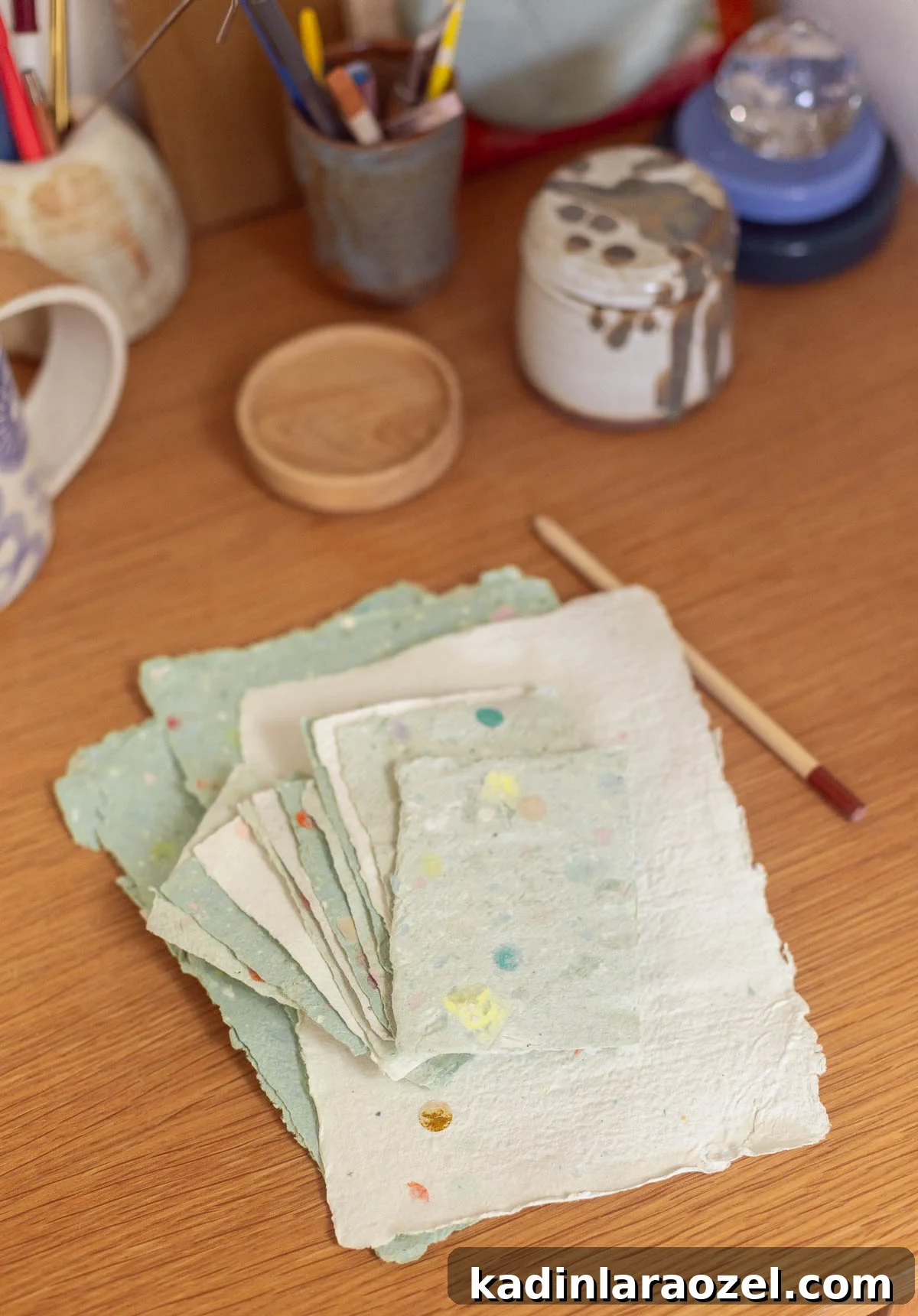 stack of homemade paper sitting on a wood desk with pencils