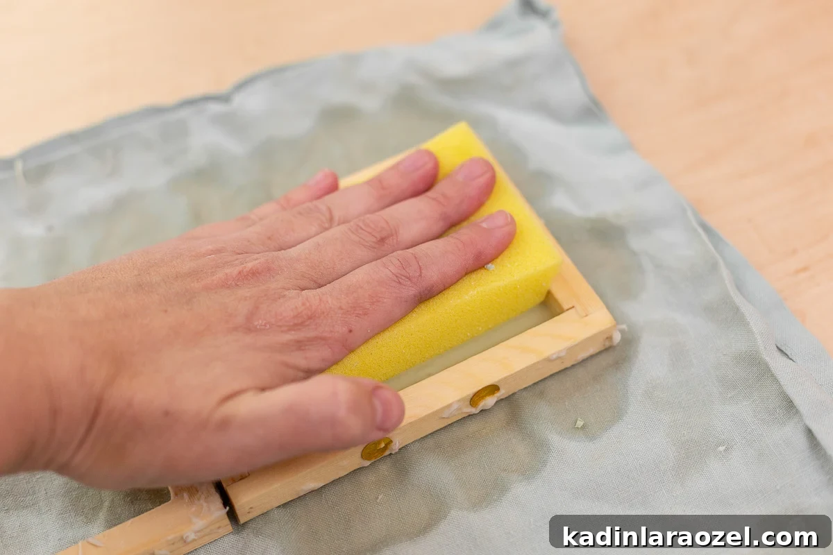 using sponge to remove excess water from sheet of paper being made