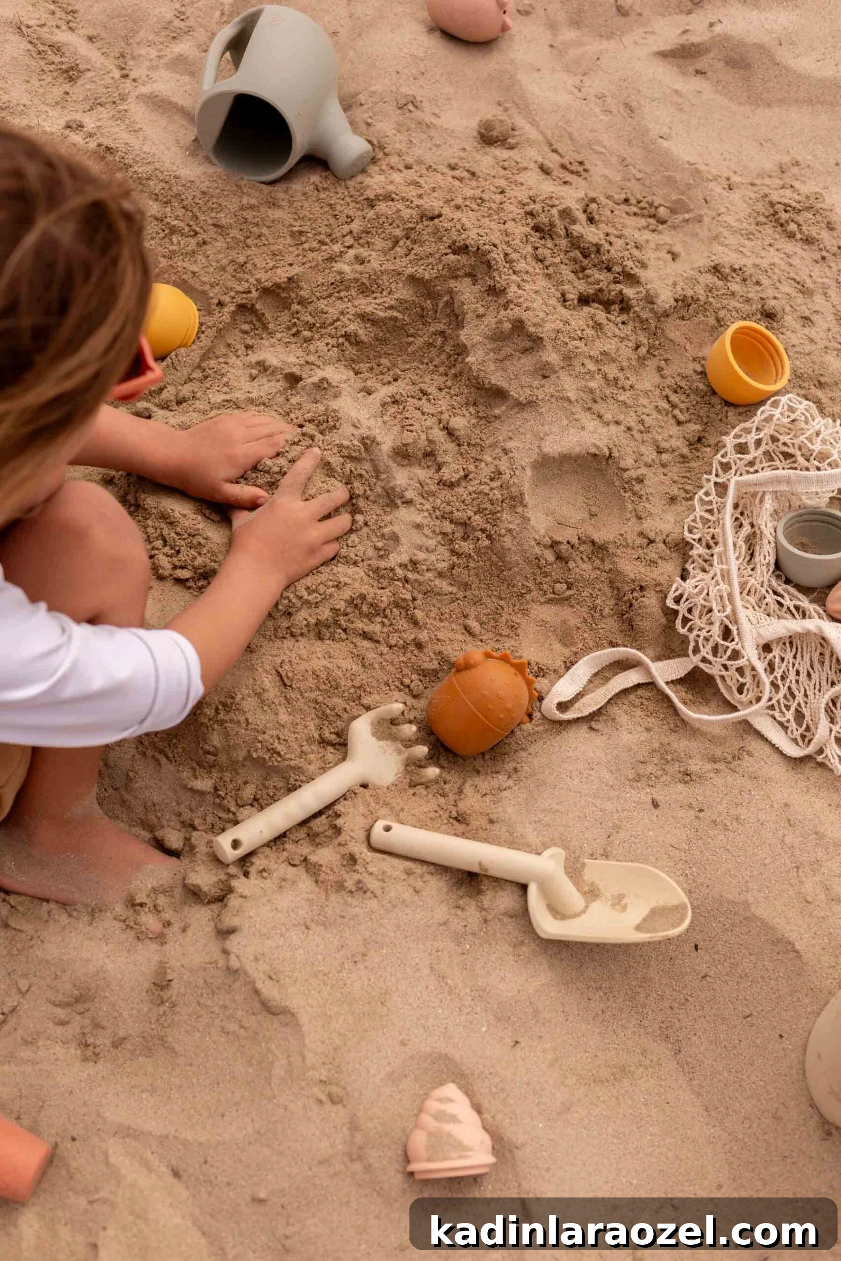 17 Fun Beach Activities for Kids and Families 6 child playing at the beach in the sand with his bands and sand toys surrounding him