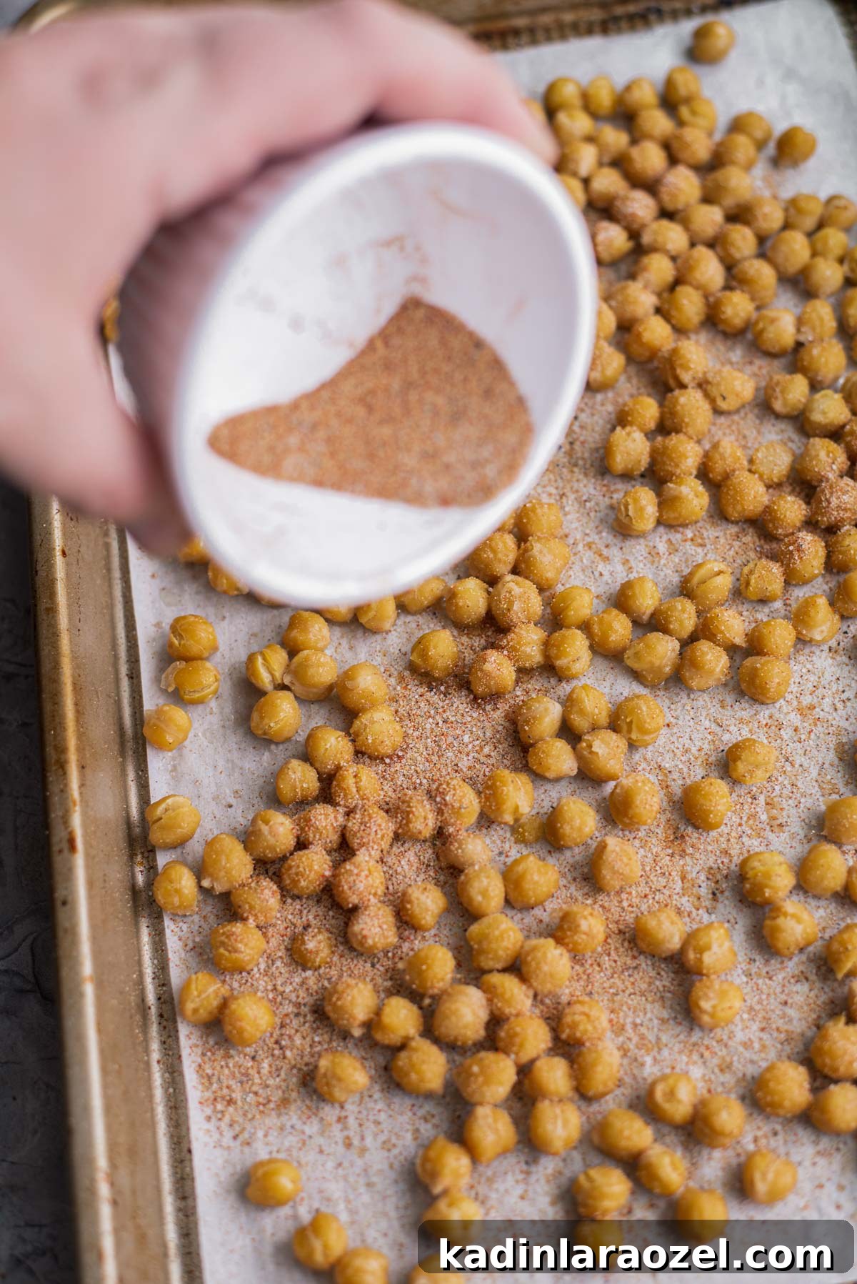 Crispy Roasted Chickpeas Recipe for Snack or Salad Topping 7 pouring spices onto roasted chickpeas that are on a baking sheet