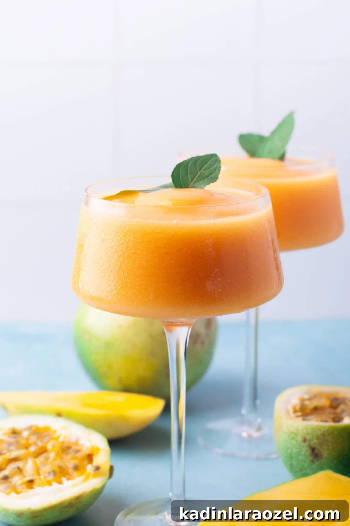 two orange frozen cocktails in tall stemware on counter with fruit