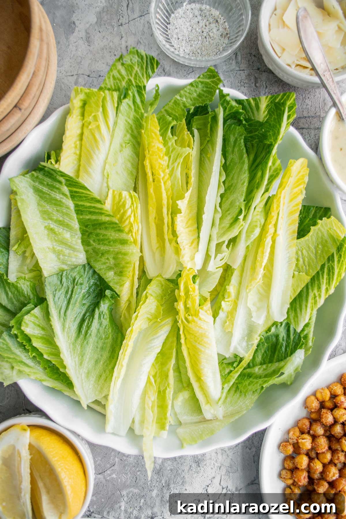 bowl of romaine and roasted chickpeas and lemons on a counter with plates and other ingredients