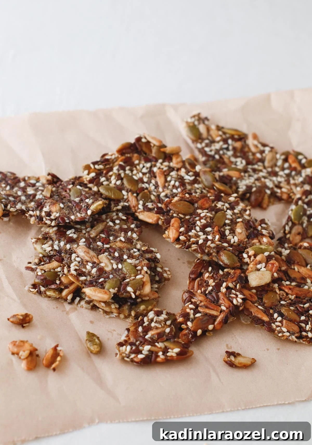 Crispy Seed Crackers Recipe: Homemade Savory Snack 2 homemade seed crackers in small pieces on a counter with wax paper underneath