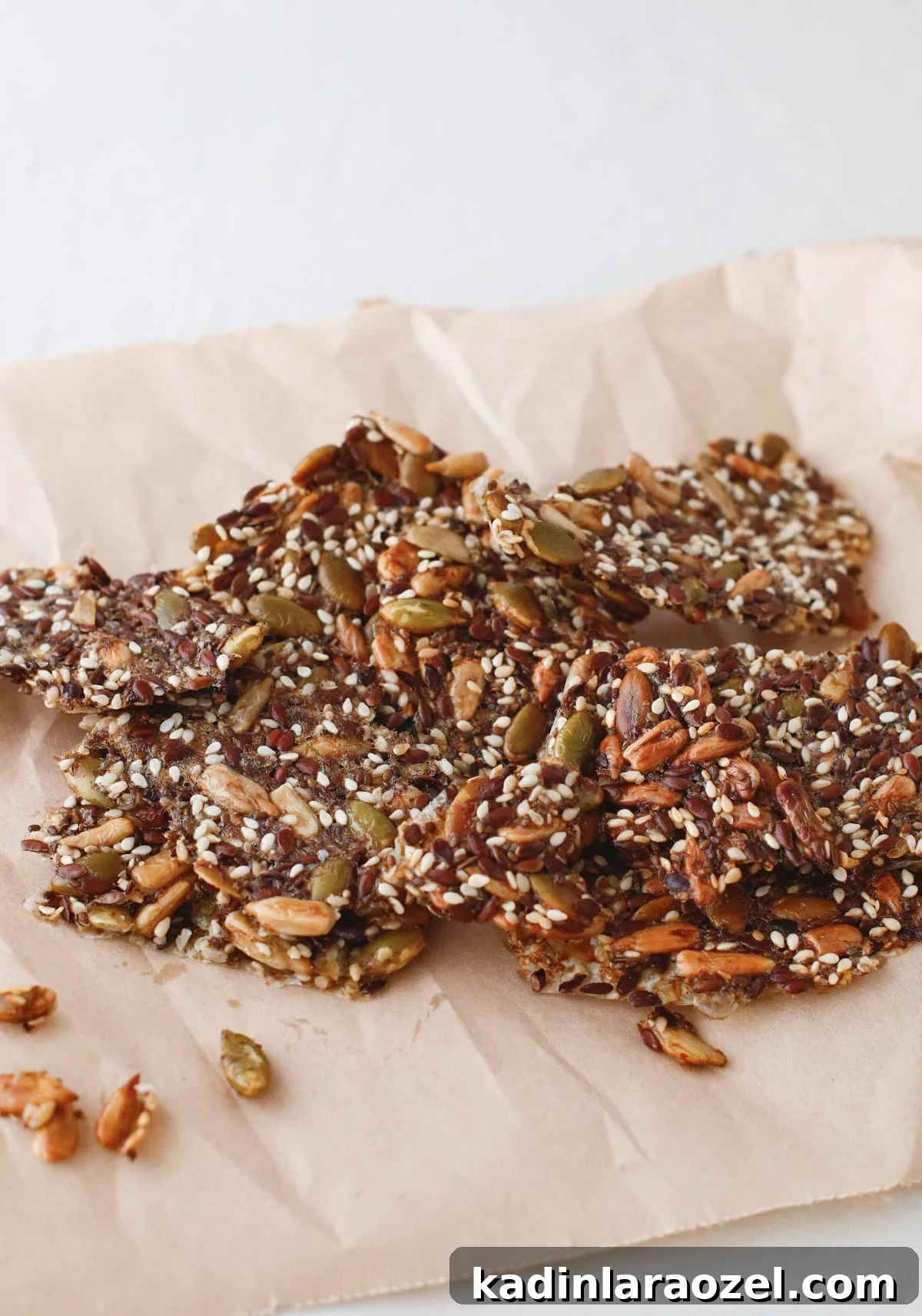 Crispy Seed Crackers Recipe: Homemade Savory Snack 12 seed crackers stacked up in a small pile, on a brown piece of wax paper