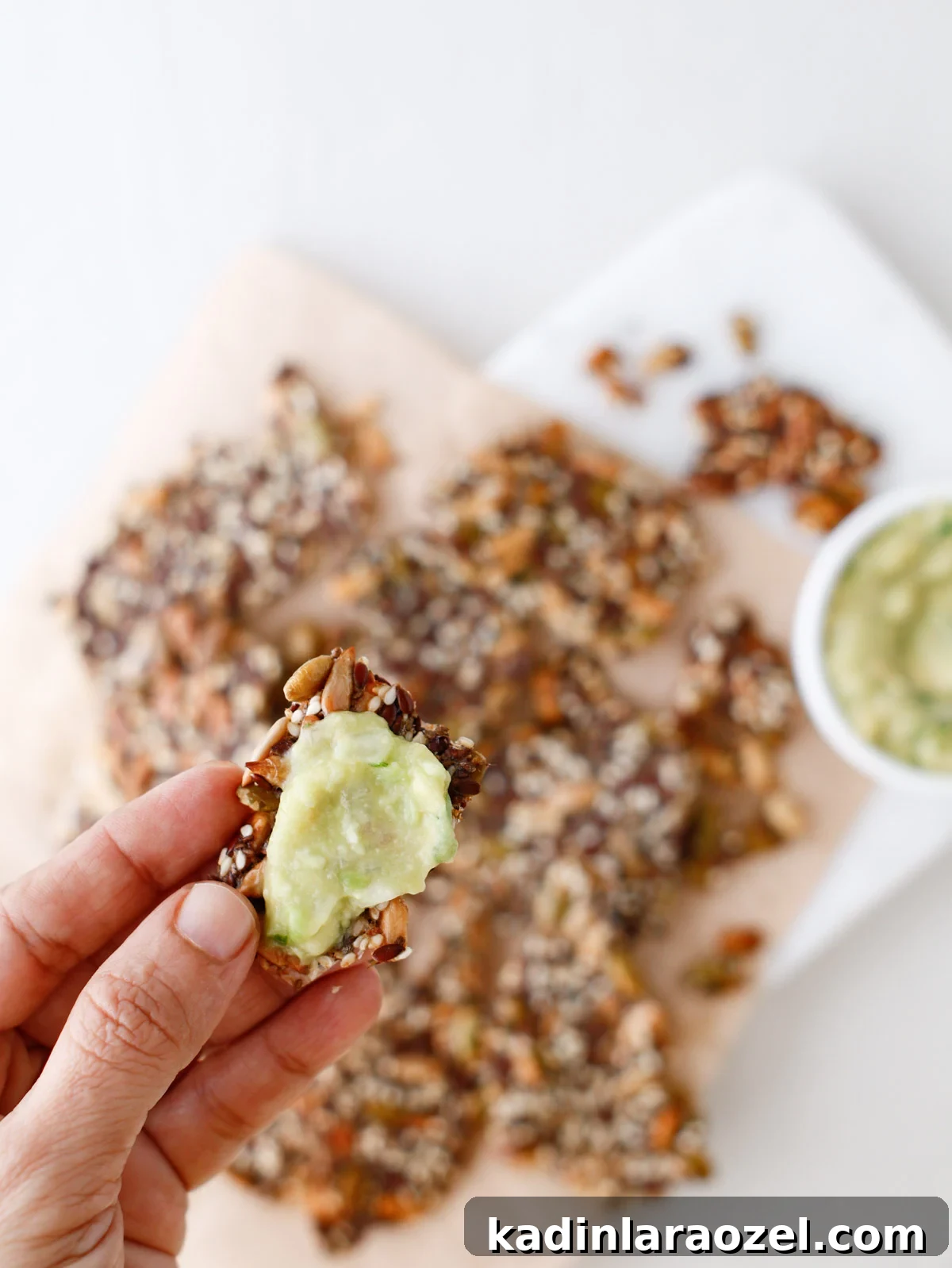 Crispy Seed Crackers Recipe: Homemade Savory Snack 13 woman's hand holding small seed cracker with green veggie dip on it