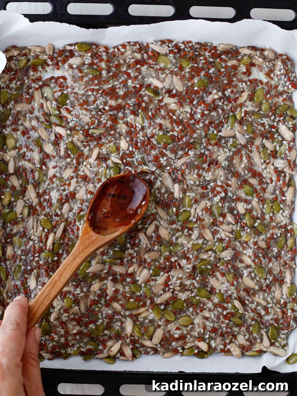Crispy Seed Crackers Recipe: Homemade Savory Snack 7 spreading seed cracker mixture out onto a sheet pan with wooden spoon