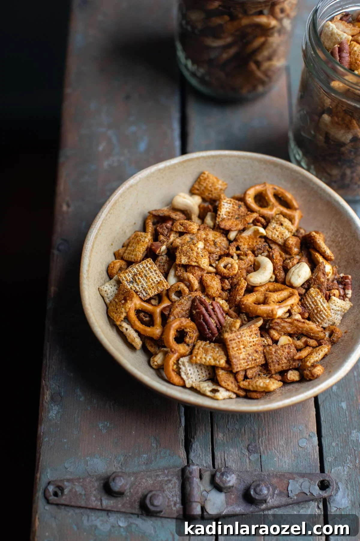 bowl of homemade chex mix with 2 small glass jars filled with chex mix behind it