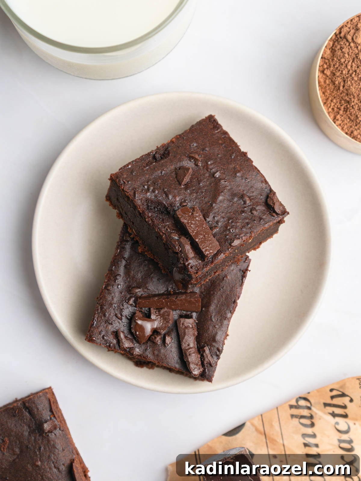 two square slices of brownie on a white plate with milk and cocoa powder