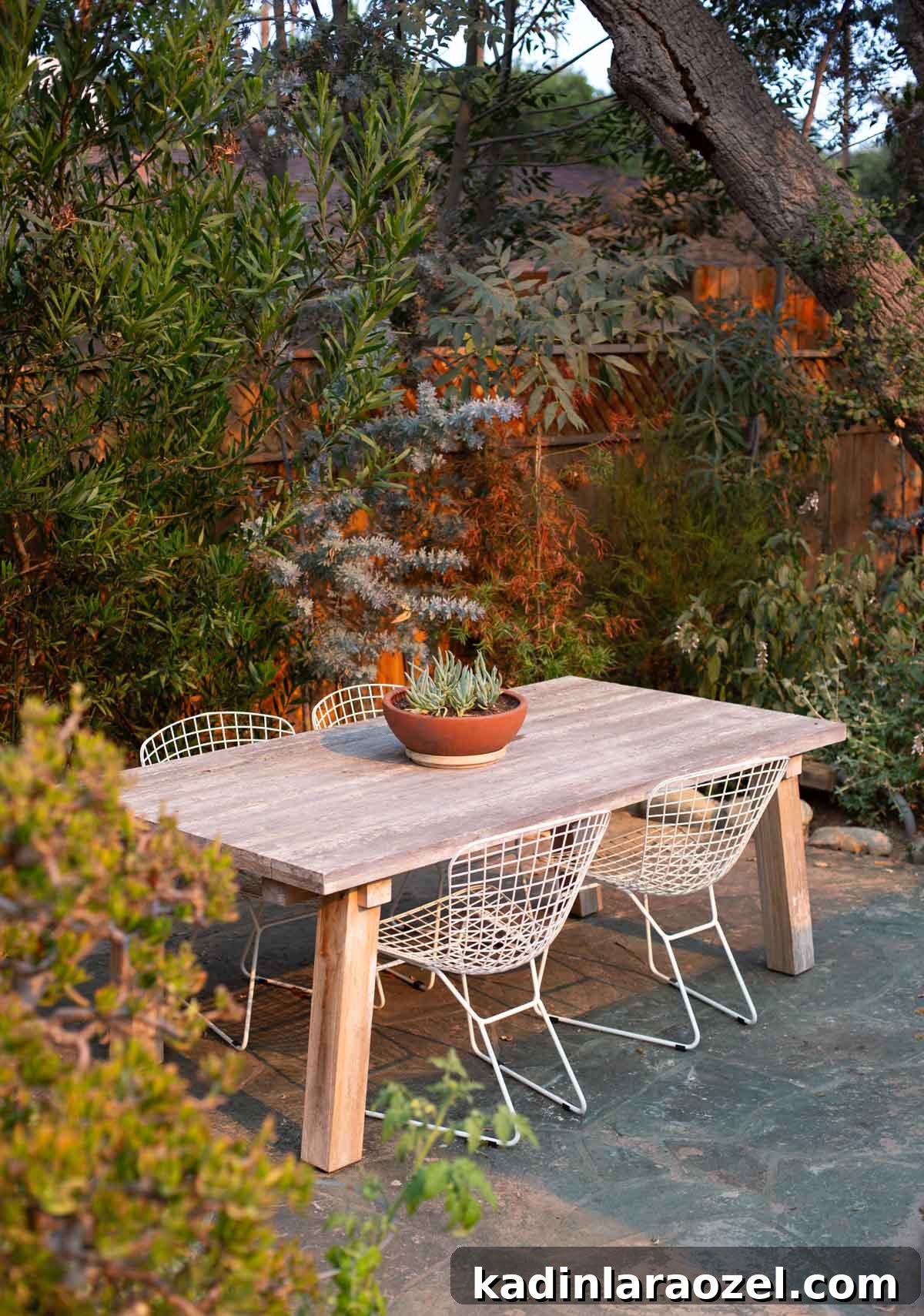 Practical Backyard Garden Ideas You Can Actually Build 21 wood outdoor dining table and modern chairs with a lush background of plants and trees behind it