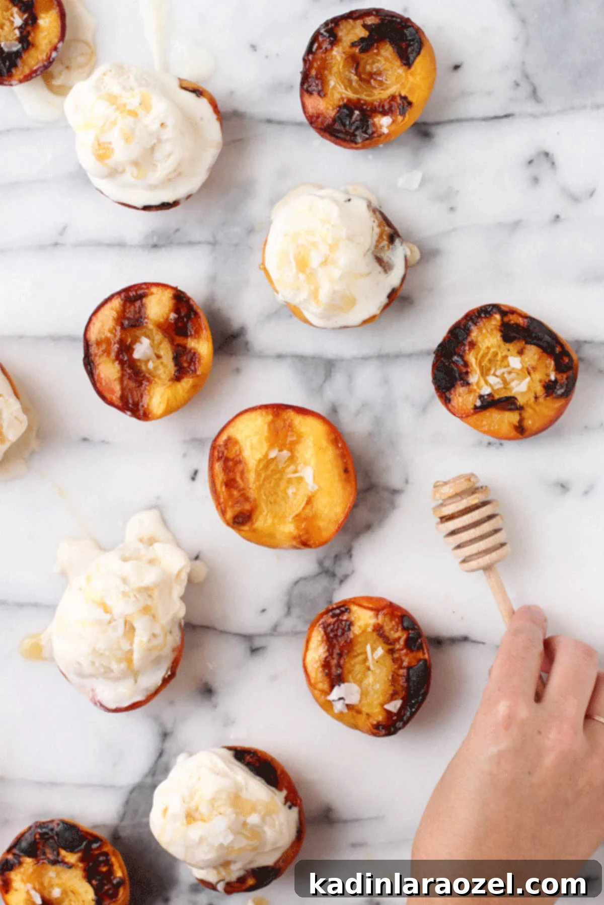Grilled peaches on marble counter, with woman's hand picking up a honey comb