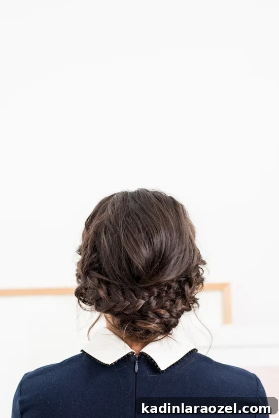 Quick Reverse Crown Braid Tutorial: Stylish Look in 15 Minutes 2 Brunette facing a white wall, with a low crown braid updo, wearing a navy blue dress
