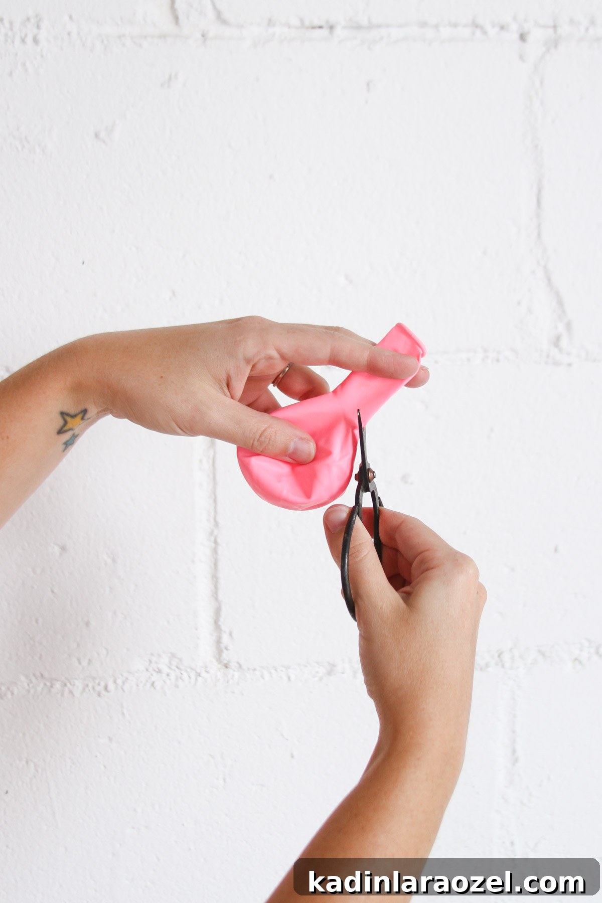 Woman's hands in front of white background, cutting the bottom off a pink balloon