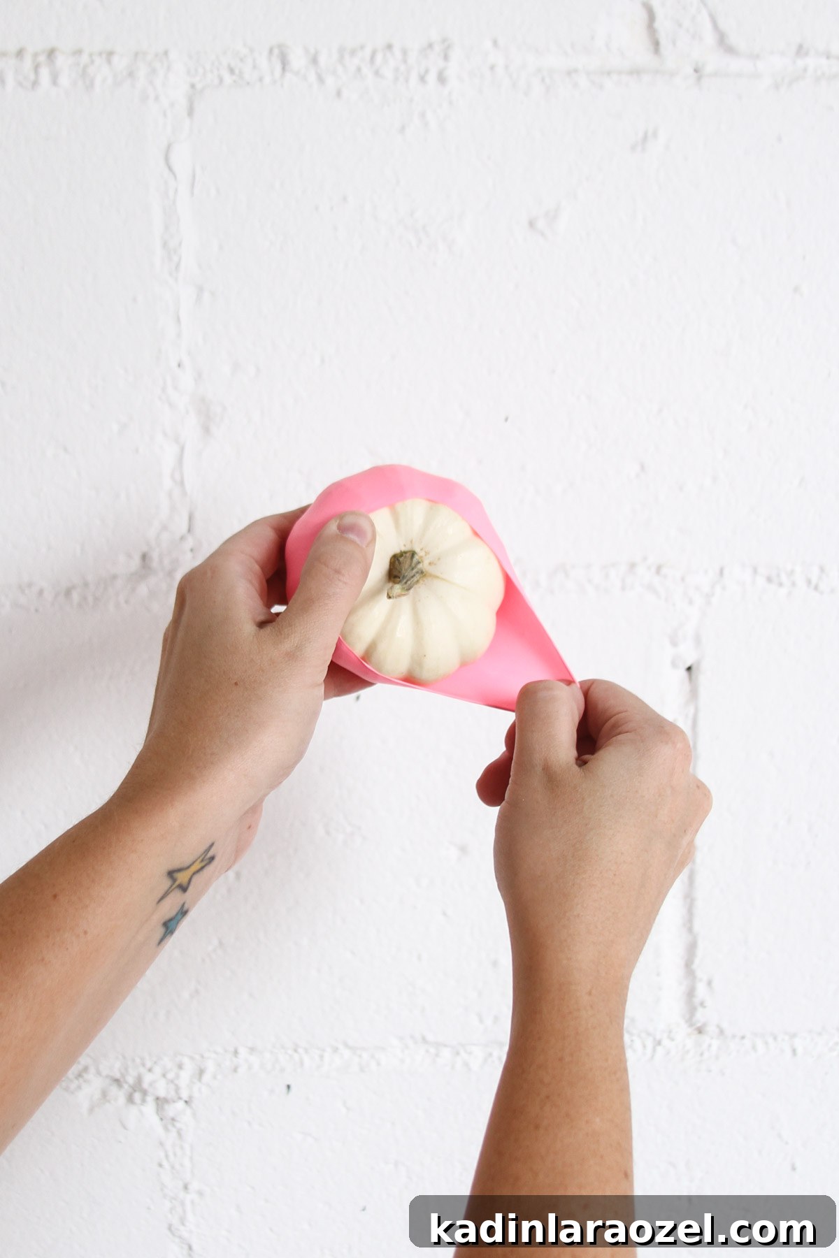 Woman's hand pulling a cut up balloon over a small white pumpkin for Halloween