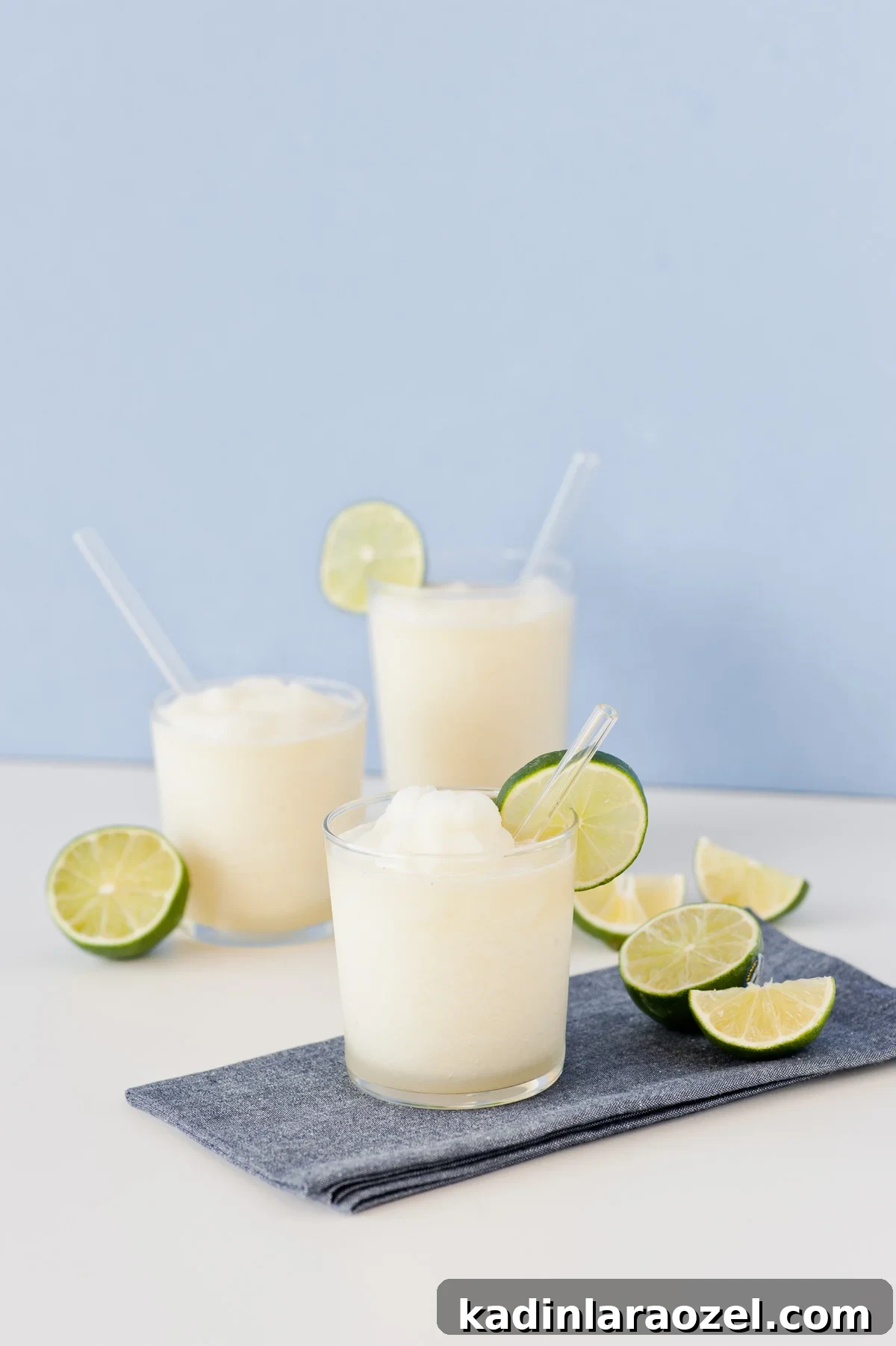 Gin and Juice Slushie Recipe: Refreshing Frozen Cocktail Guide 5 White colored slushie cocktails with lime wedges on blue background