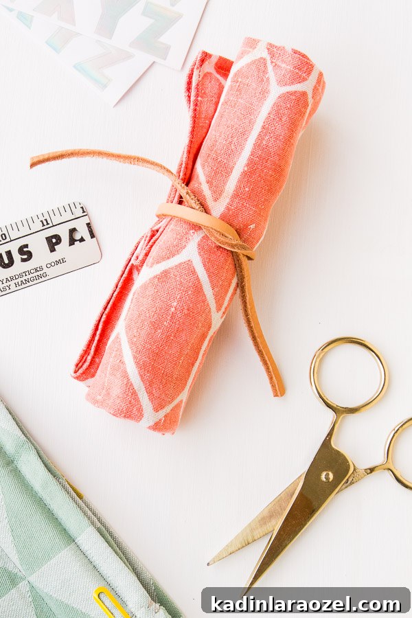 Pink pattern rollup fabric organizer with leather cord on a white desk.