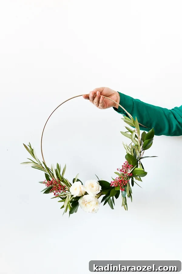 Create an Asymmetrical Wreath: Step-by-Step Design Guide 10 DIY holiday wreath being held up with olive branches, white flowers, and red berries