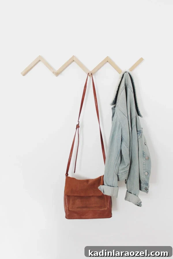 49 Clever DIY Home Organization Ideas to Maximize Space 32 A wood zig zag coat rack hangs on a white wall with a jean jacket and a brown purse.
