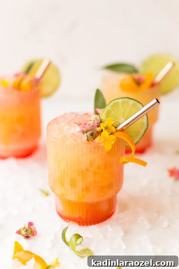 pineapple mango rum punch in a clear ribbed glass with orange zest garnish and edible flowers
