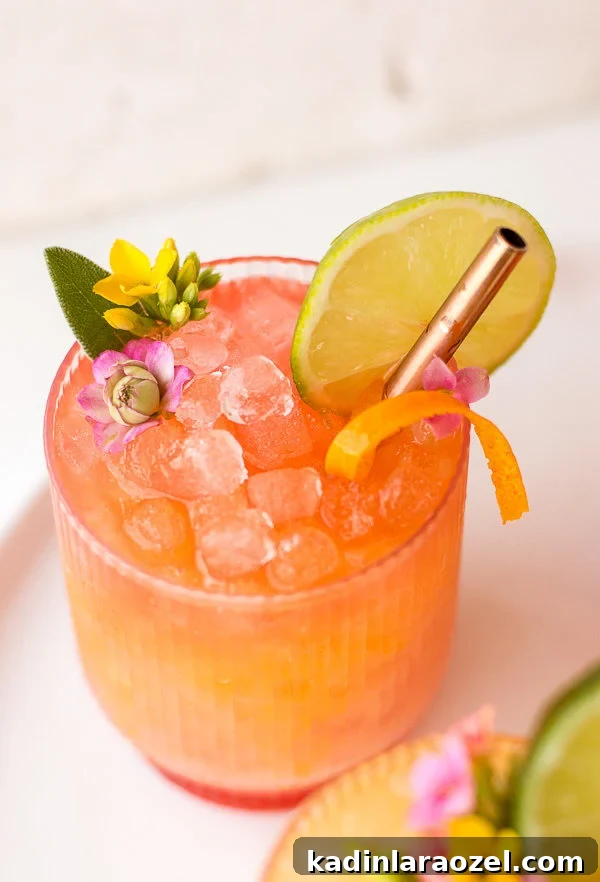 Pineapple mango rum punch in a clear glass with nugget ice and edible flower garnish