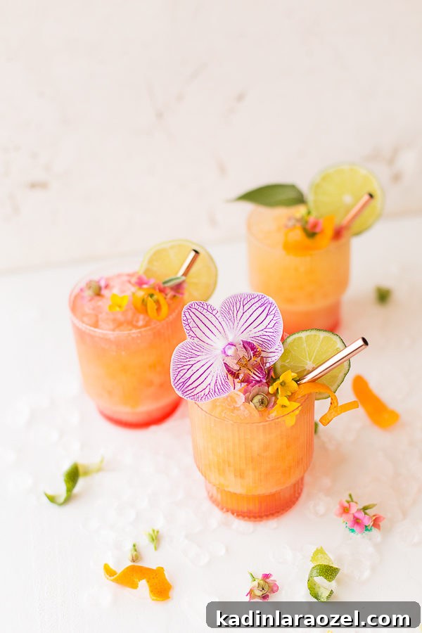 three orange and red cocktails with crushed ice and edible flowers on top