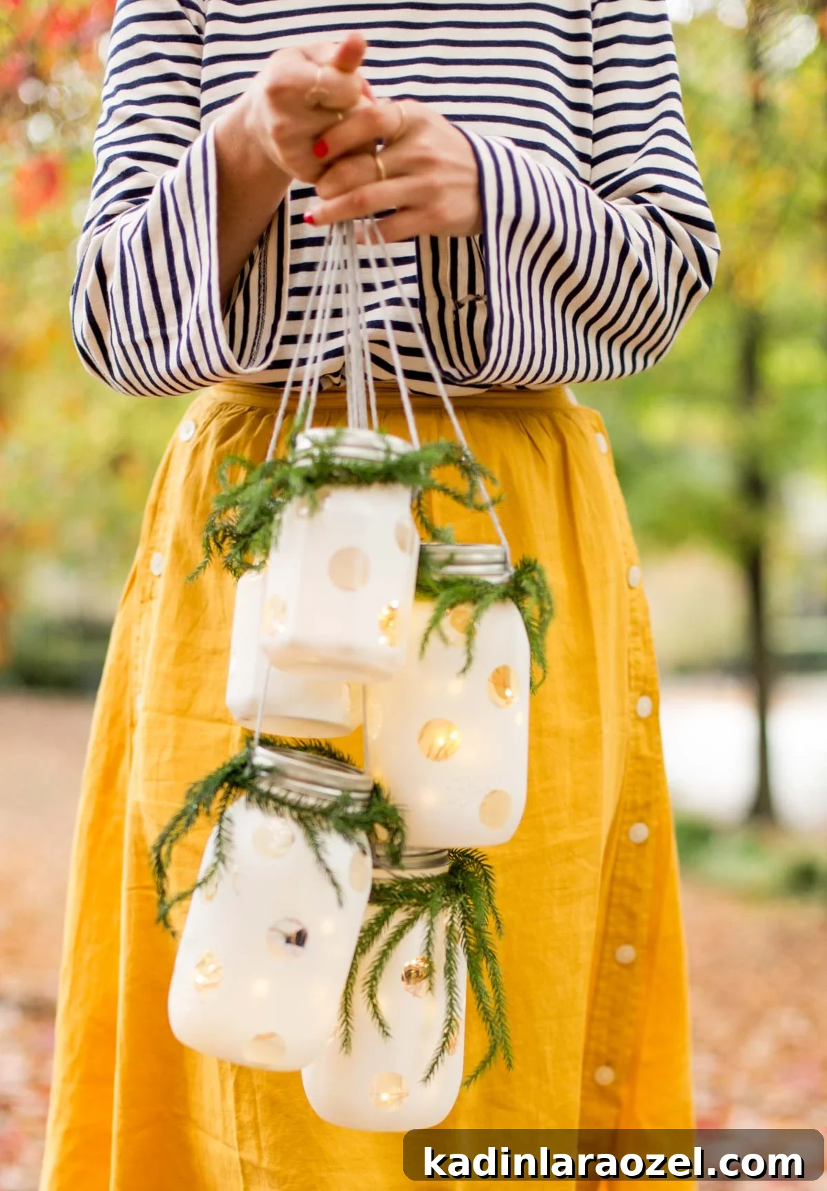 Woman wearing striped long sleeve shirt holding Christmas hanging lanterns in front of her, with Christmas garland