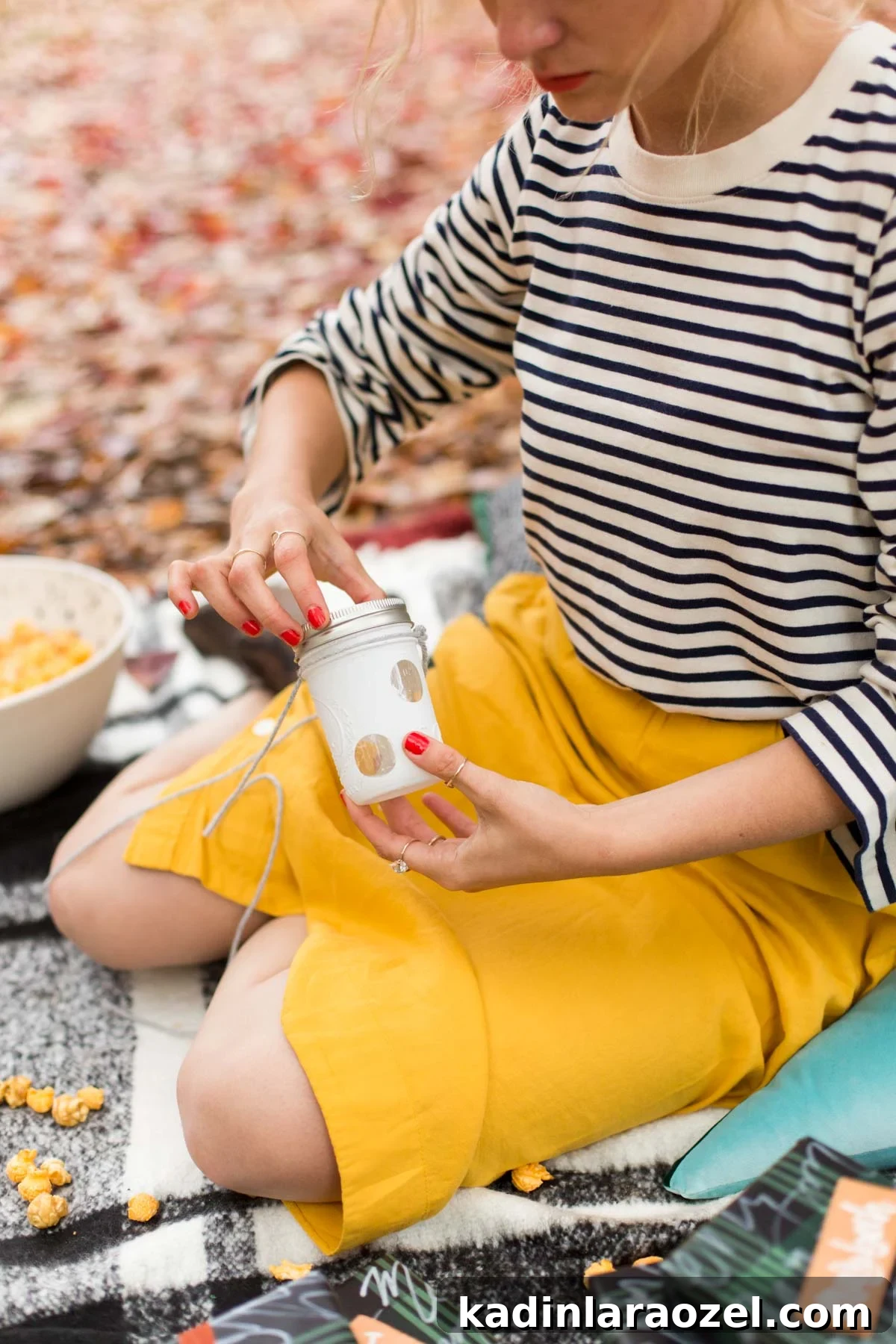 Woman holding DIY Christmas lanterns, sitting on cozy picnic blanket 