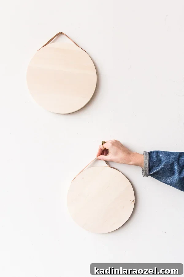 10-Minute DIY Leather Handle Serving Tray Tutorial 6 woman's hand hanging up two minimal wood trays on a white wall