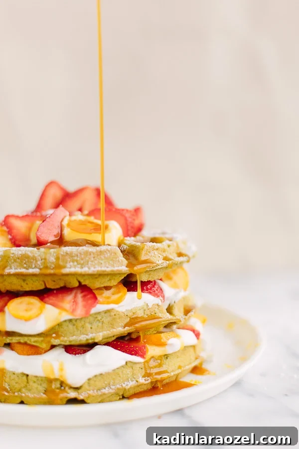 Matcha Waffles Recipe: Fluffy Green Tea Waffles with Crispy Edges 2 closeup of green matcha waffles with whipped cream, strawberries, and syrup dripping down the waffle stack