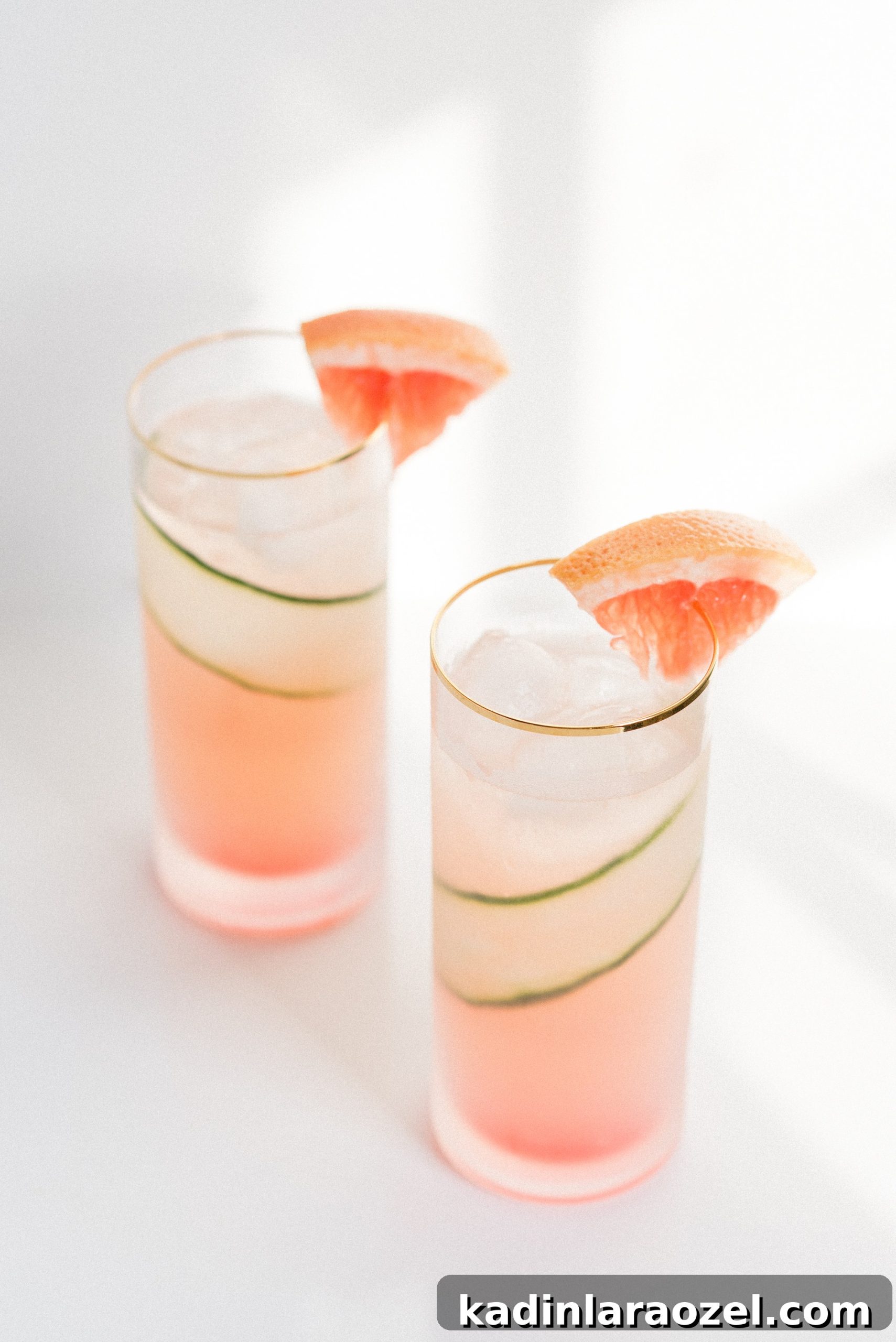 two highball glasses of pink cocktails with grapefruit and cucumbers
