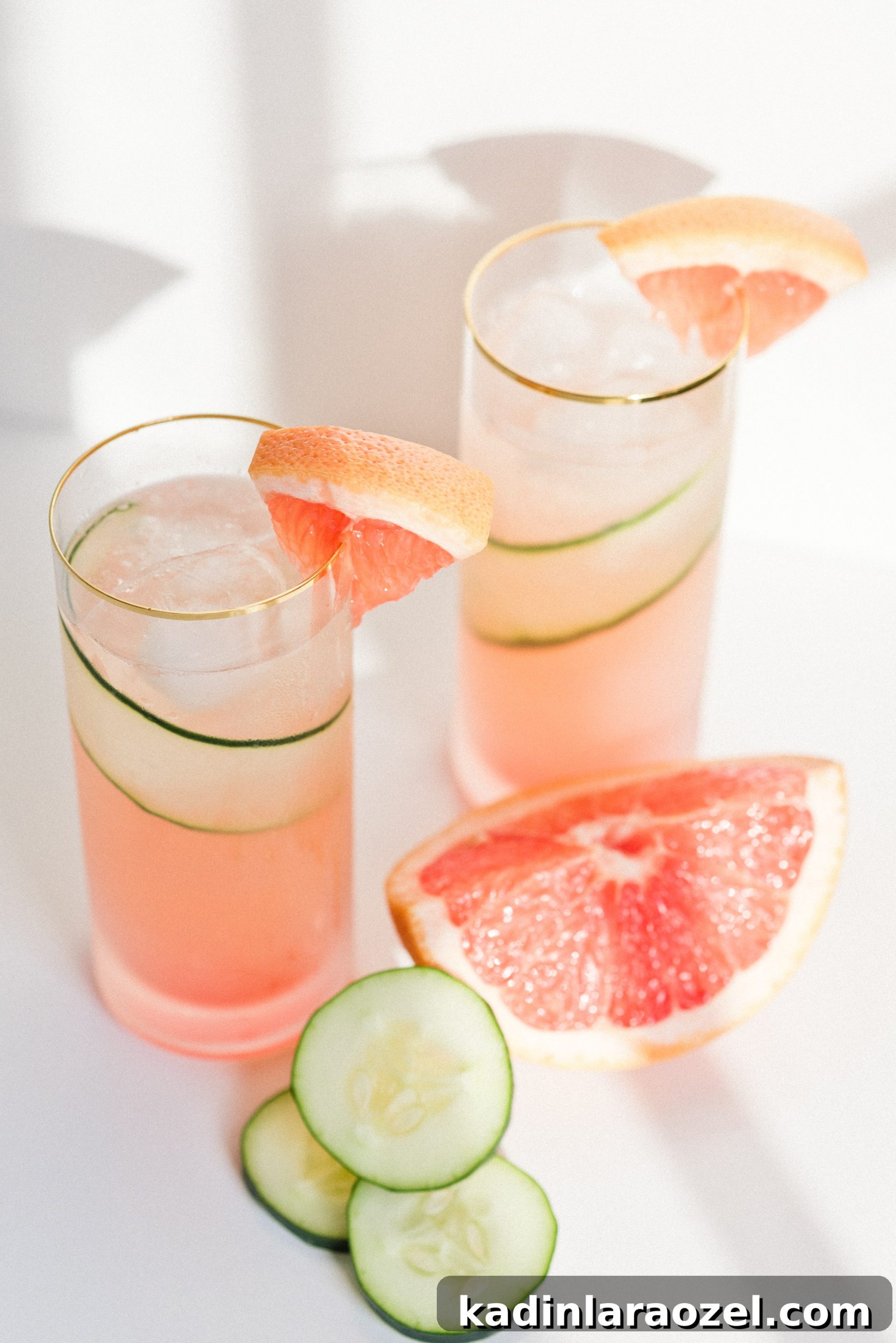 Pink grapefruit cucumber gin cooler with two glasses and slices of cucumber and grapefruit