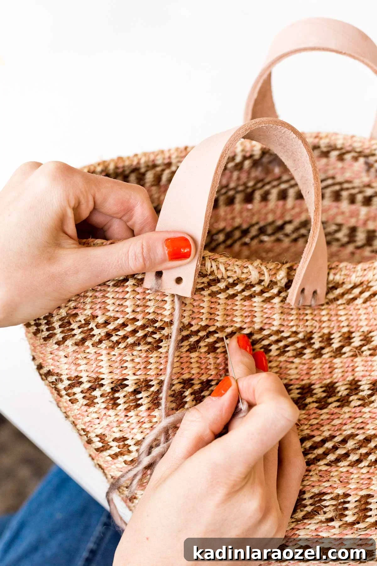 Stitch leather handle onto striped woven basket that is brown and pink