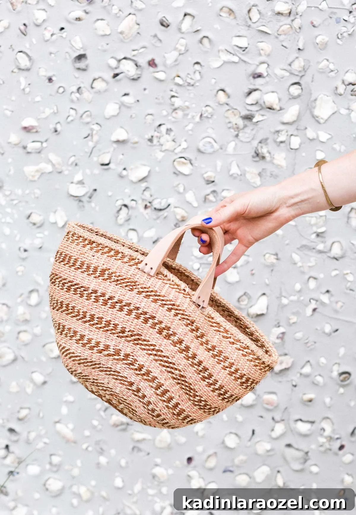 Woman holding striped basket bag in front of a shell wall