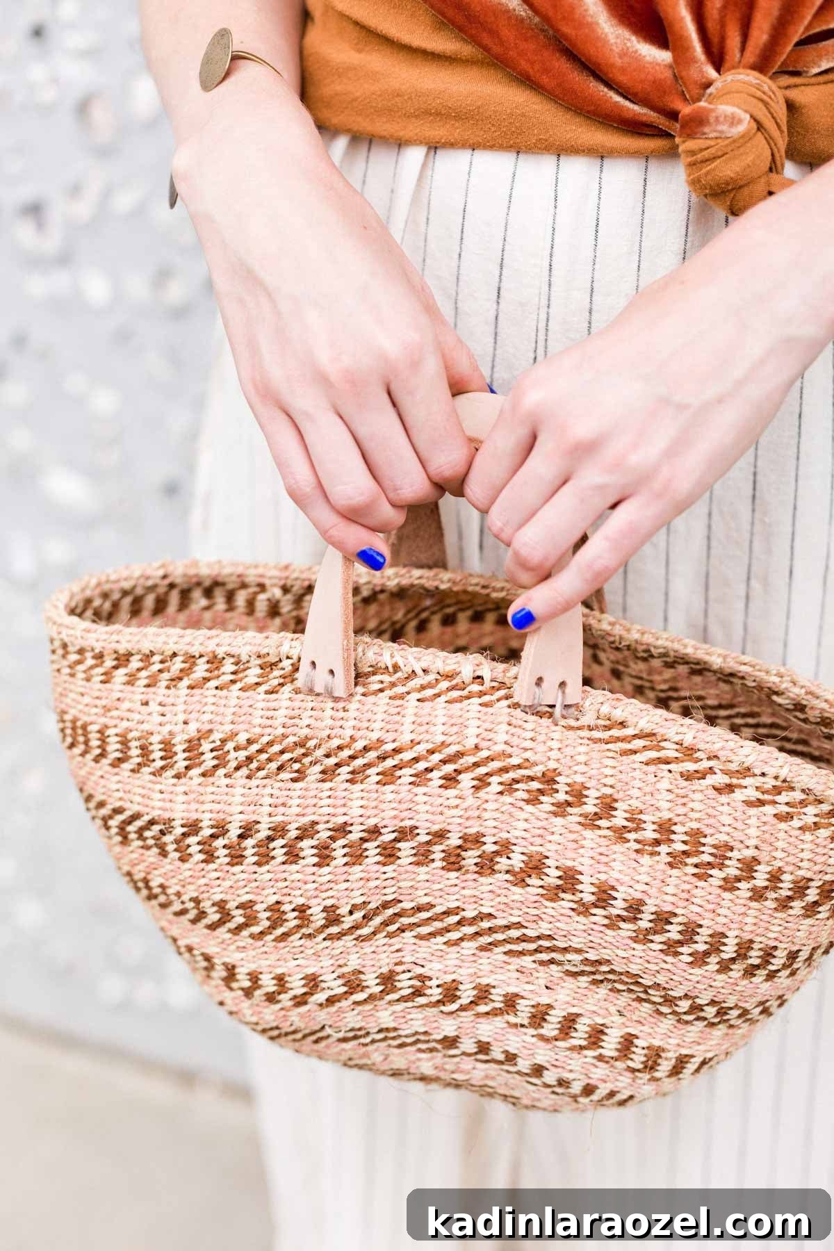 Woman holding stripes basket bag in front of her, wearing a neutral summer outfit