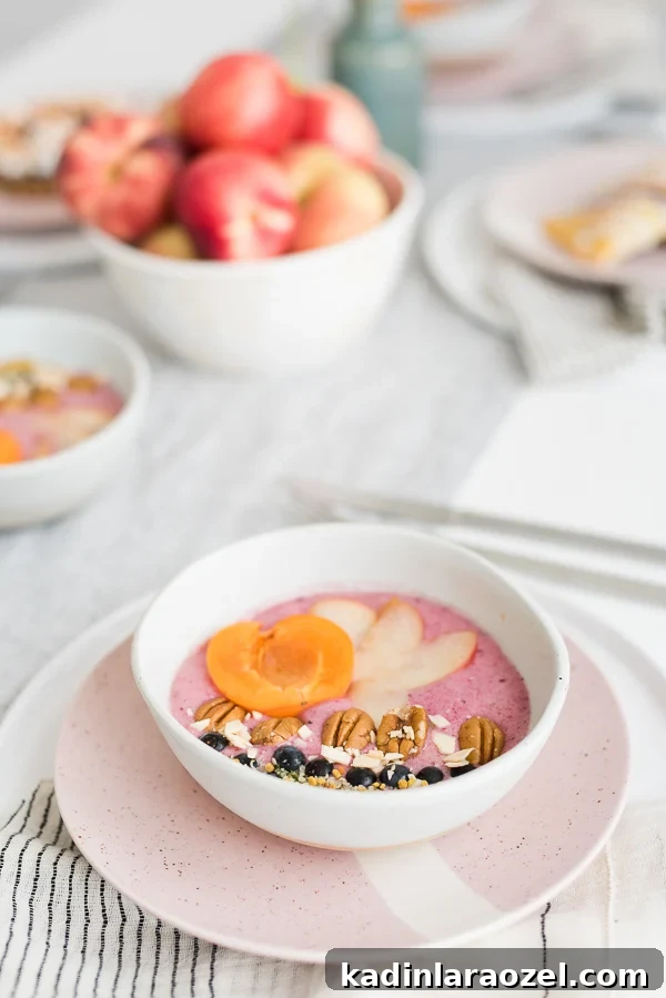 2-Ingredient Smoothie Bowls You Can Make in Minutes 4 Pink smoothie bowl with fruit and nuts on top, sitting on white linen table.