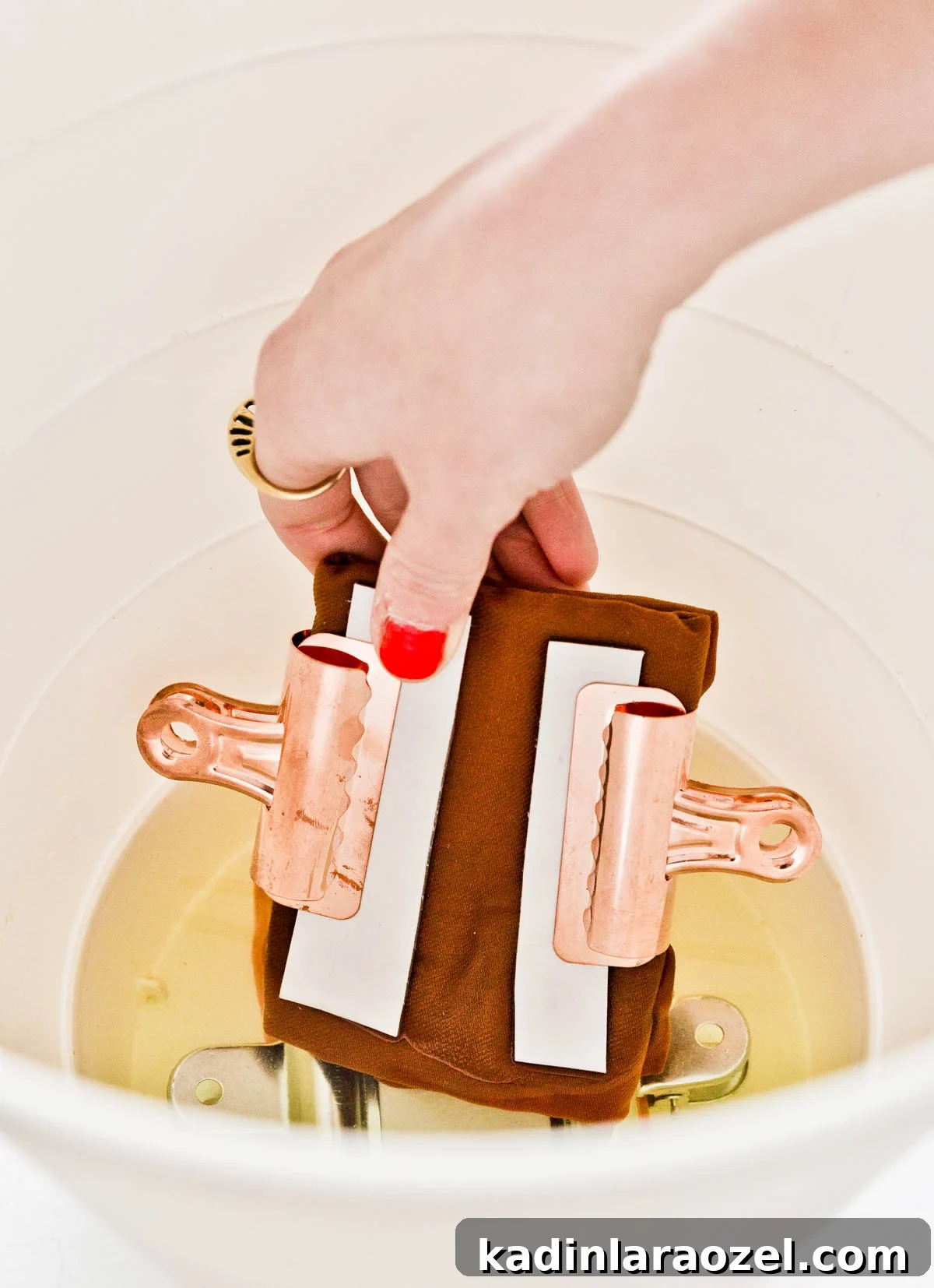 Dipping brown fabric napkins into bleach with two metal clips attached to create a bleached tie dye effect.