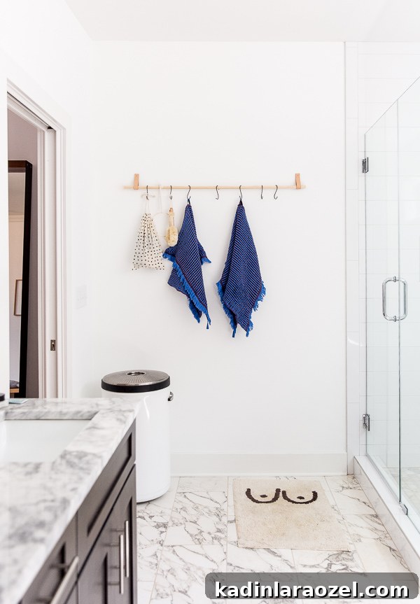 Modern bathroom with marble floors and counters, featuring a minimal wood rail wall organizer for towels and bathroom accessories
