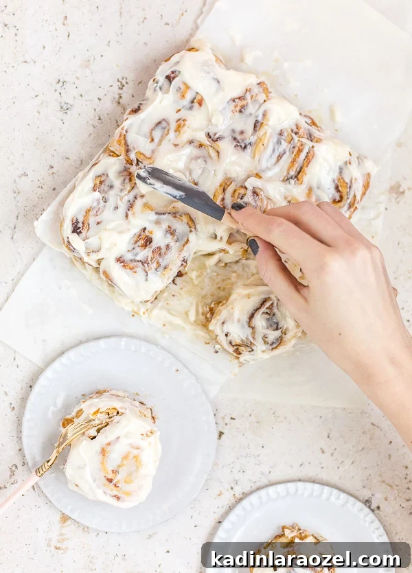 11 Irresistible Fall Recipes You’ll Crave This Season 9 pumpkin cinnamon rolls being iced with cream cheese frosting, on a stone countertop