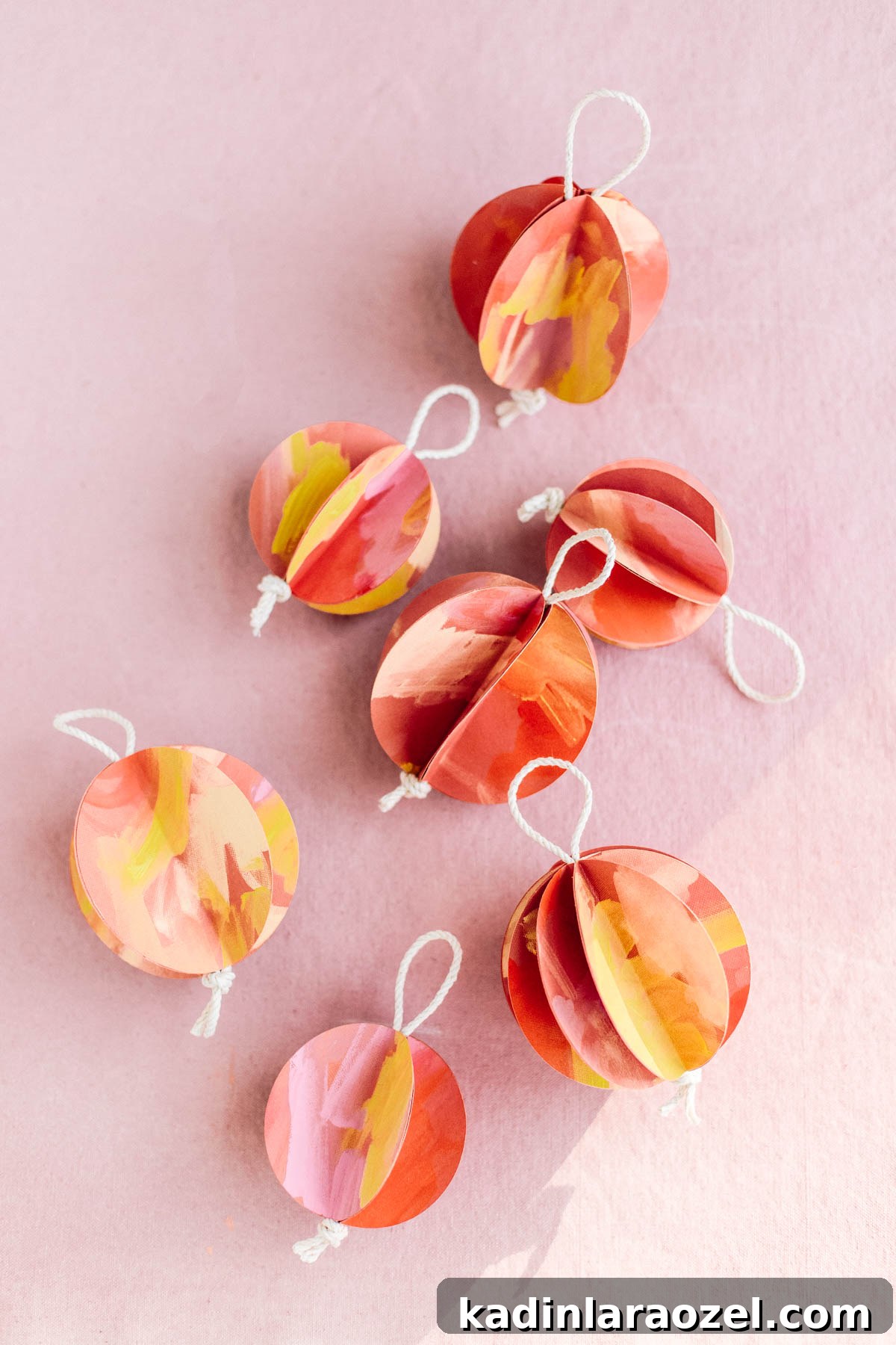 Red, pink, and yellow painted 3D ball ornaments resting on pink backdrop for the holidays