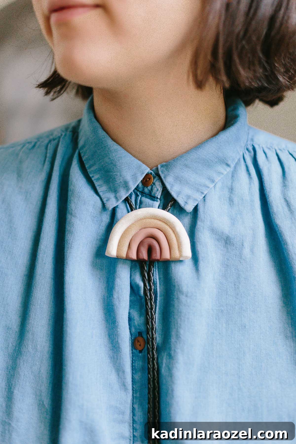 Clay rainbow bolo tie being worn by woman wearing blue collared shirt.