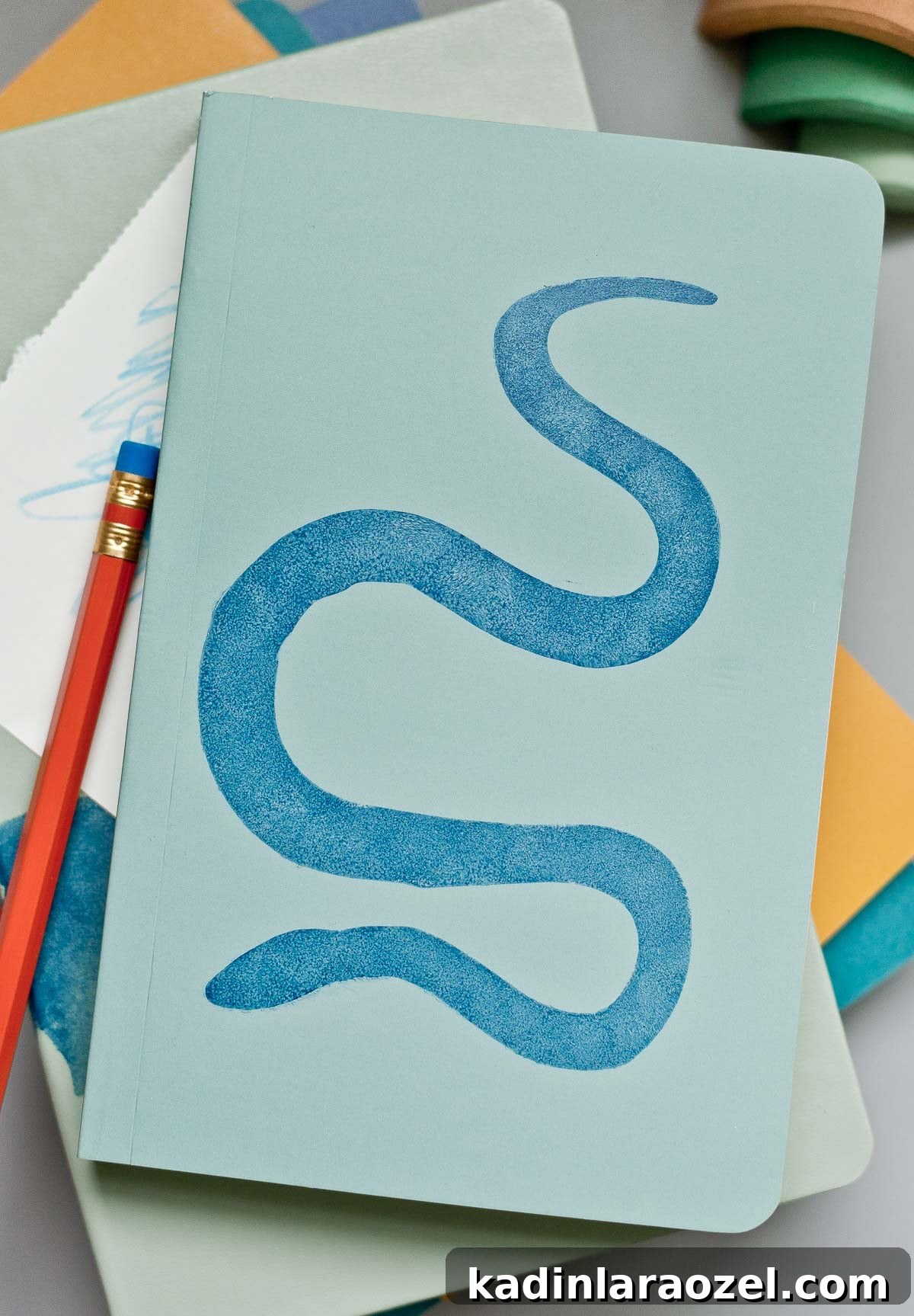3 Stylish Back-to-School DIY Projects That Impress 5 Stack of colorful notebooks with a blue snake design on top and red pencil next to it