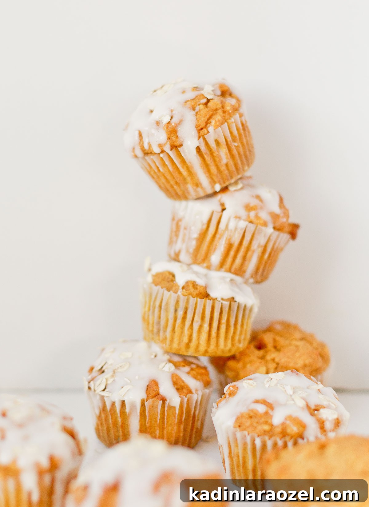 Simple Delicious Pumpkin Muffins Recipe You’ll Love 7 Pumpkin muffins stacked on top of each other, with a cream cheese glaze and oats sprinkled on top.