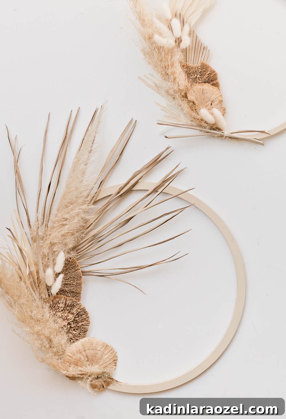 Two modern asymmetrical fall wreaths - made of pampas grass, wheat, and palm leaves.