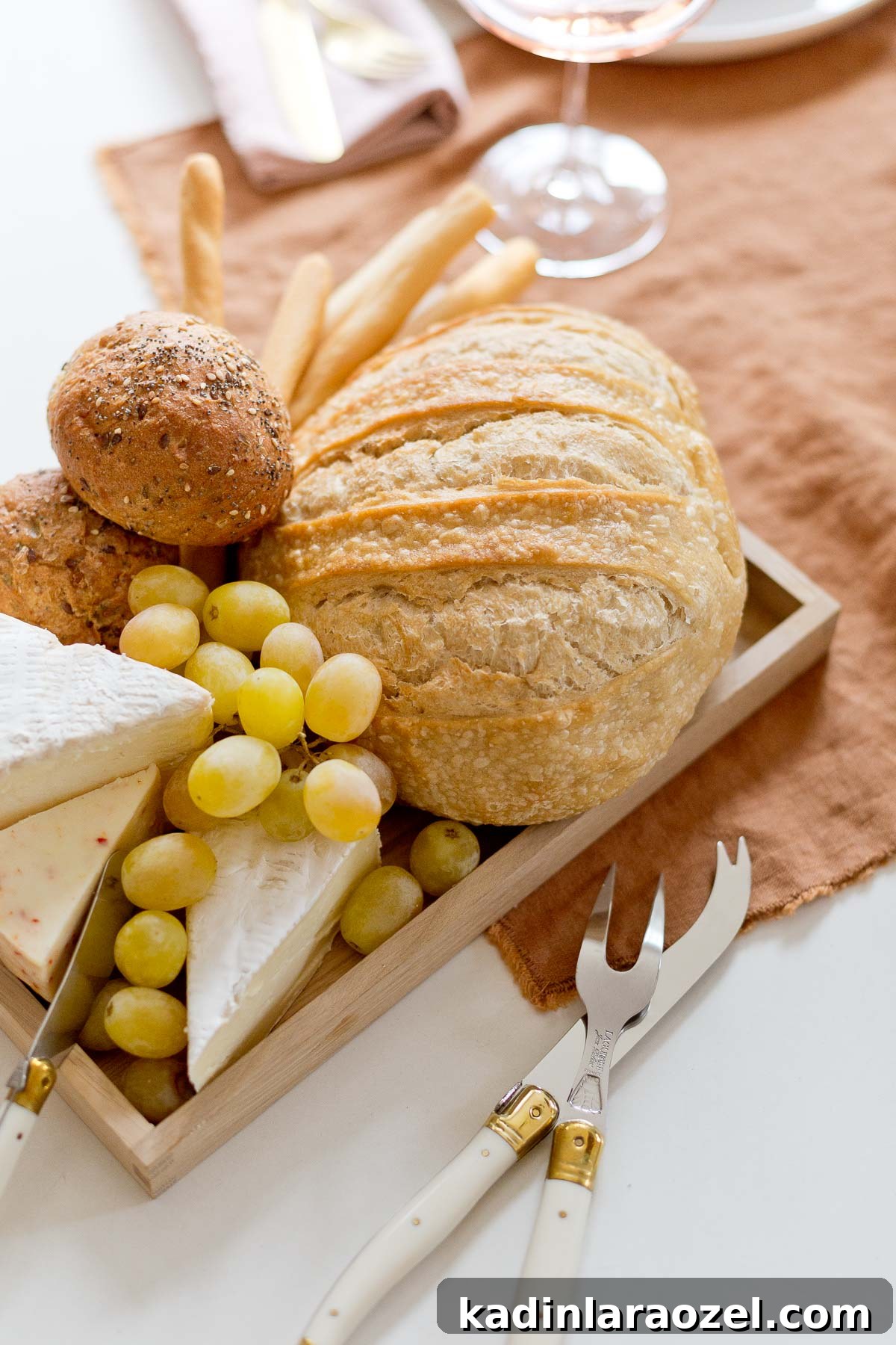 Bread tray with slices of cheese and grapes on a rust colored table runner