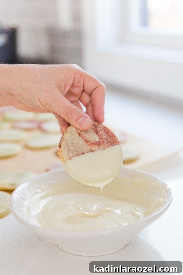 Dipping marbled sugar cookies into bowl of melted white chocolate