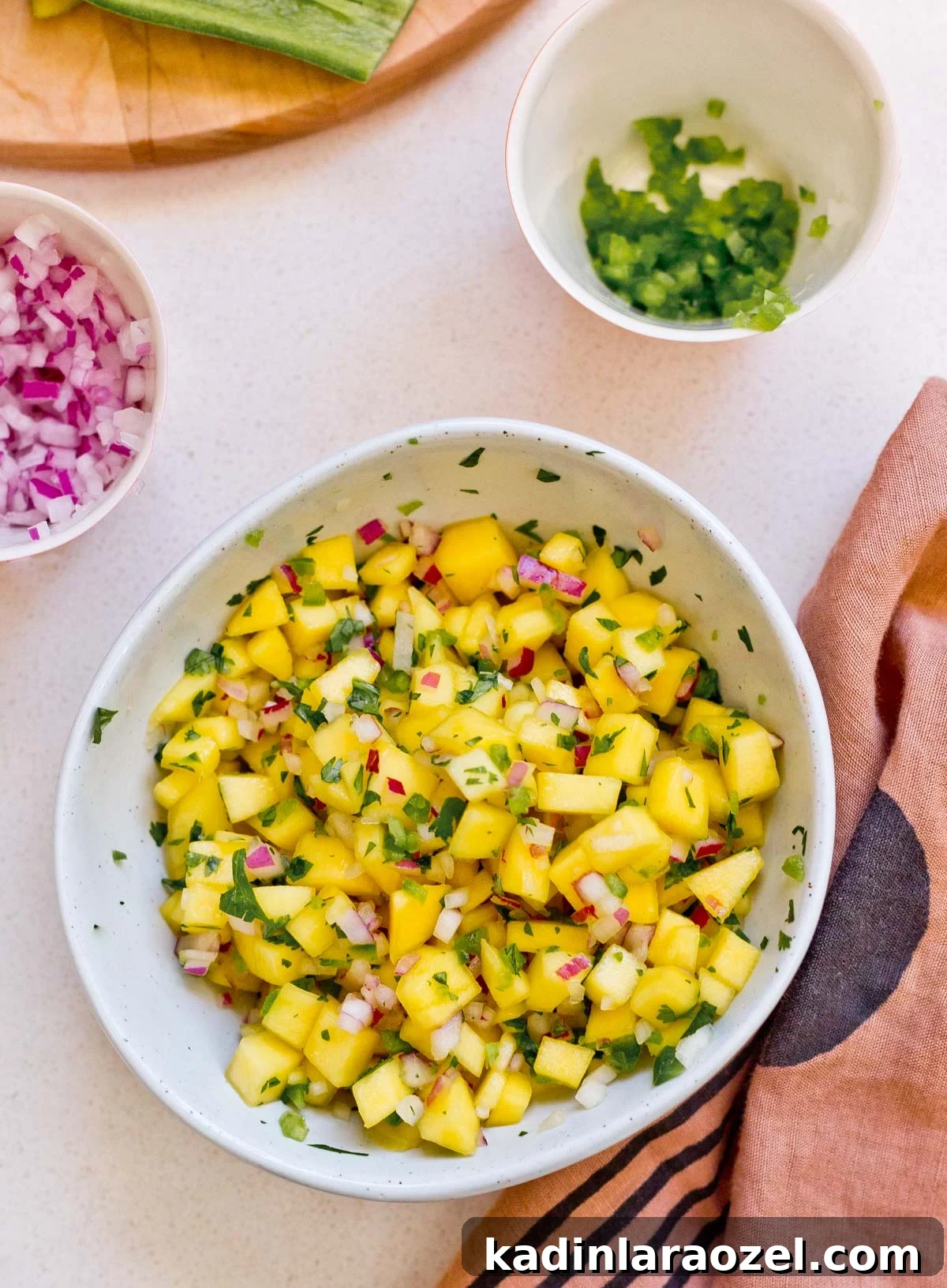 mango salsa in white bowl on table, surrounded by ingredients 